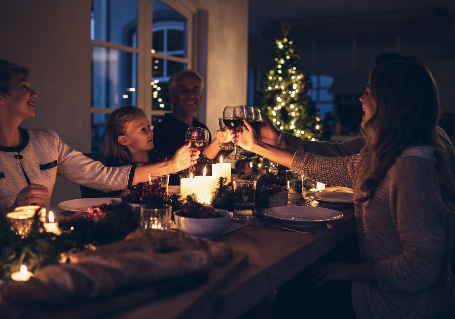 Eine Familie sitzt an der weihnachtlich dekorierten Tafel und stößt gemeinsam an.